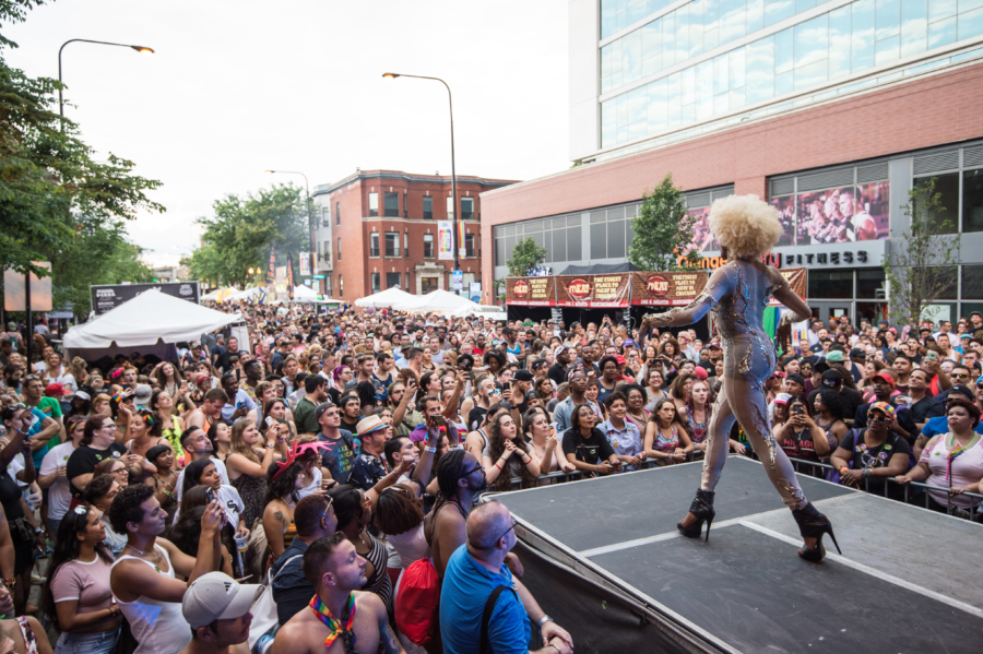 Drag performer entertains a large, cheering crowd at Chicago Pride Fest in Northalsted, on a stage set against the city’s urban backdrop.